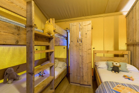 Interior de la tienda Lodge Safari en Sandaya Etruria, Italia, con literas de madera y juguetes infantiles.