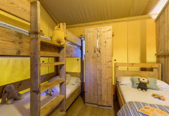 Interior de la tienda Lodge Safari en Sandaya Etruria, Italia, con literas de madera y juguetes infantiles.