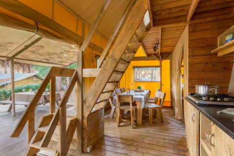 Interieur van een safaritent met houten trap en eetruimte in Lodge Oasi, Sandaya Etruria, Italië.