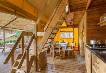 Interior of a safari tent with wooden stairs, dining area and kitchen at Lodge Oasi, Sandaya Etruria, Italy.