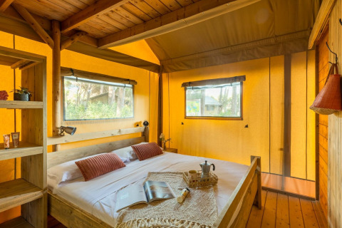 Cozy bedroom with wooden bed and windows inside the Lodge Oasi safari tent at Sandaya Etruria in Italy.