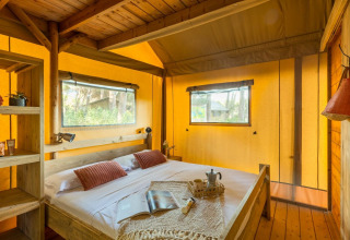 Cozy bedroom with wooden bed and windows inside the Lodge Oasi safari tent at Sandaya Etruria in Italy.