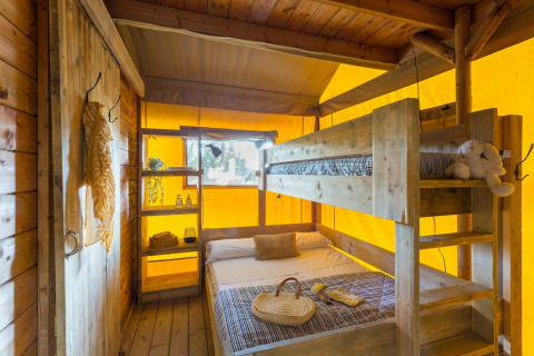 Interior view of Lodge Oasi safari tent at Sandaya Etruria in Italy, featuring bunk beds and wood decor.