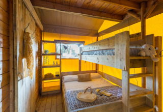 Interior view of Lodge Oasi safari tent at Sandaya Etruria in Italy, featuring bunk beds and wood decor.
