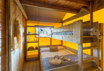 Interior view of Lodge Oasi safari tent at Sandaya Etruria in Italy, featuring bunk beds and wood decor.