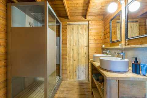 Modern wooden bathroom with double sinks, mirrors, and shower in Lodge Oasi, Sandaya Etruria, Italy.