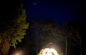 Le dôme Skydome Ushuaïa éclairé au Camping Domaine de la Faurie en France, la nuit, entouré d’arbres.