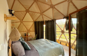 Vue intérieure du Skydome Ushuaïa au Camping Domaine de la Faurie en France, avec lit confortable et fenêtres en dôme.
