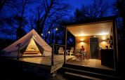 Vue nocturne du tipi et de la terrasse éclairés de la tente Nomad au Camping Domaine de la Faurie, France.