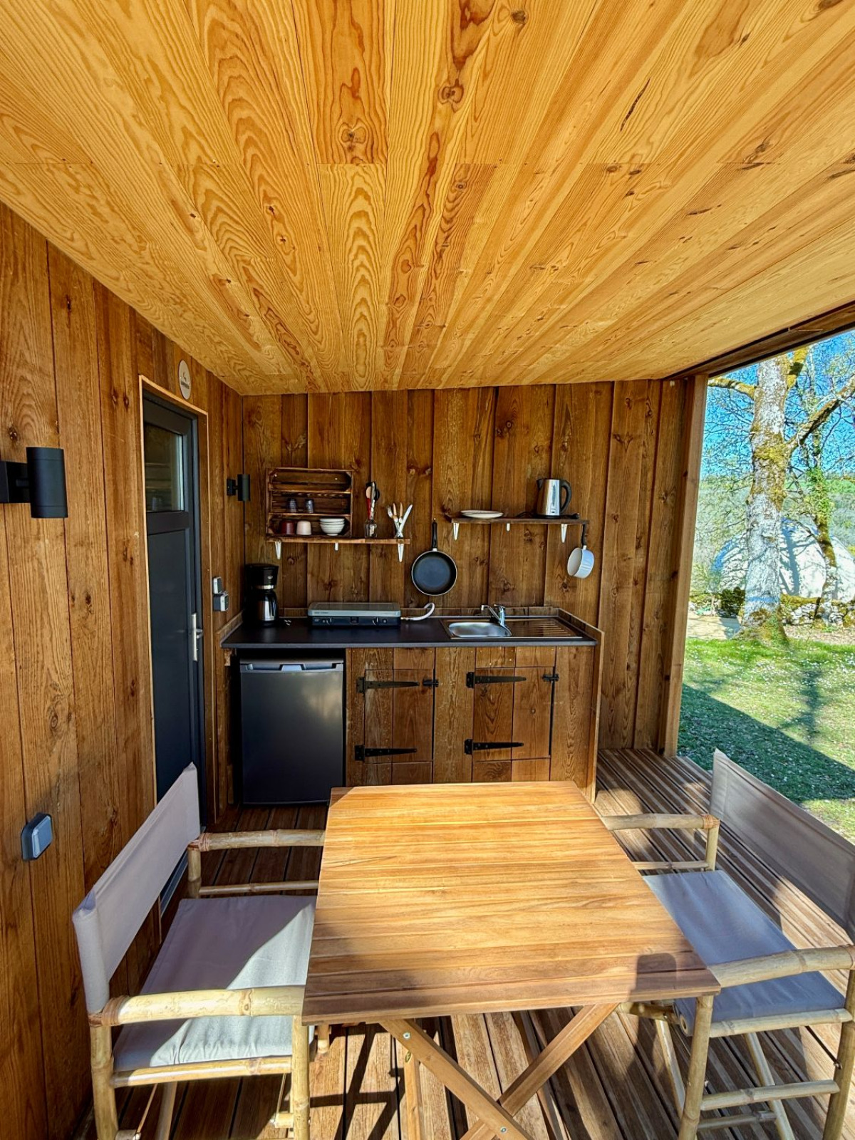 Houten kookhoek en eethoek in Tent Nomad bij Camping Domaine de la Faurie, Frankrijk, met uitzicht op de natuur.