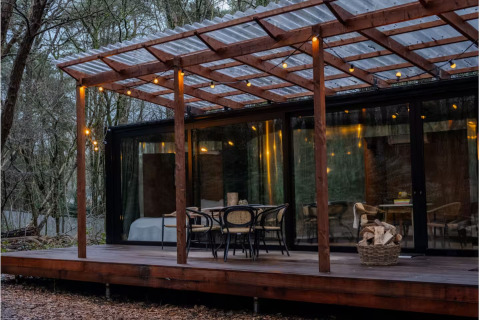 Outdoor deck at Slowlodge Echo lodge featuring wooden furniture, string lights, and large forest view windows.