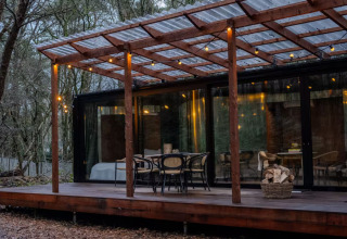 Outdoor deck at Slowlodge Echo lodge featuring wooden furniture, string lights, and large forest view windows.