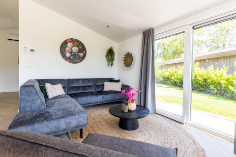 Salon moderne à la Villa Waterzicht Luxe avec sauna, canapé d’angle et grandes fenêtres donnant sur le jardin à Molenvelden.