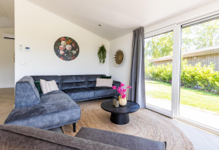 Soggiorno moderno di Villa Waterzicht Luxe con sauna, divano angolare e vista giardino a Molenvelden, Olanda.