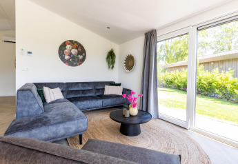 Modern living room at Villa Waterzicht Luxe with sauna, corner sofa, large windows and garden view in Molenvelden.