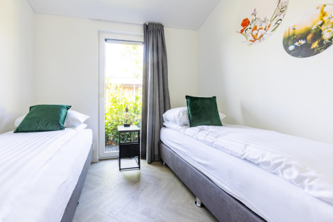 Moderne tweepersoonskamer met groene kussens, veel licht, wanddecoratie en tuinzicht in Villa Waterzicht Luxe.
