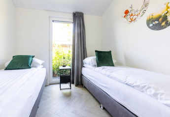Chambre moderne à deux lits, coussins verts, lumière naturelle et décor floral à la Villa Waterzicht Luxe.