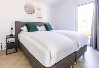 Camera moderna con letto matrimoniale, cuscini verdi e arte murale a Villa Waterzicht Luxe con Sauna nei Paesi Bassi.