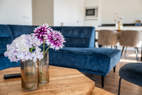 Flores en un jarrón sobre una mesa de madera con un sofá azul en Villa Waterzicht Comfort, Molenvelden, Países Bajos.