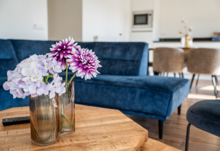 Flores en un jarrón sobre una mesa de madera con un sofá azul en Villa Waterzicht Comfort, Molenvelden, Países Bajos.