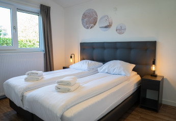 Modern twin bedroom with white linens, bedside lamps and wall art at Villa Waterzicht Comfort, Molenvelden.
