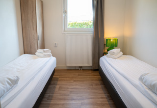 Værelse med to enkeltsenge, træskab og grøn lampe på Villa Waterzicht Comfort, Holiday park Molenvelden.
