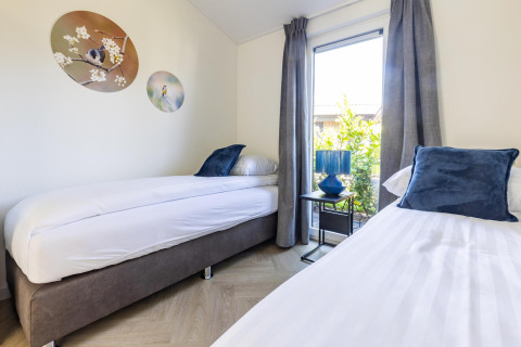 Modernes Schlafzimmer mit zwei Einzelbetten, blauen Kissen und Fenster in Villa Waterzicht Luxe 4.