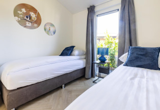 Modernes Schlafzimmer mit zwei Einzelbetten, blauen Kissen und Fenster in Villa Waterzicht Luxe 4.