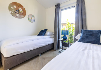 Tweepersoonskamer met blauwe kussens, grote ramen en wanddecoratie in Villa Waterzicht Luxe 4.
