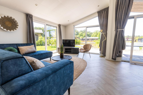 Helles Wohnzimmer in der Villa Waterzicht Luxe 4 im Holiday Park Molenvelden, mit blauer Couch und Blick nach draußen.