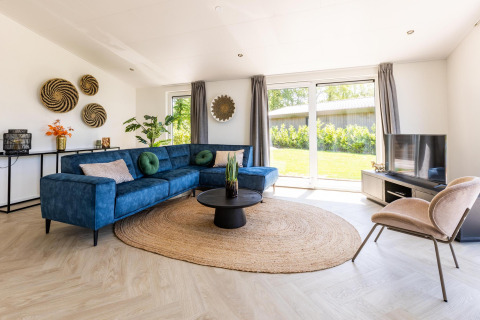 Soggiorno luminoso con divano angolare blu, decori murali rotondi e vista giardino a Villa Waterzicht Luxe 4.