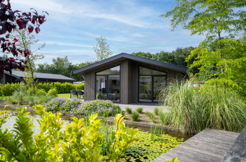 Villa Waterzicht Luxe 6 en Holiday park Molenvelden, rodeada de vegetación y un estanque tranquilo.