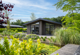 Villa Waterzicht Luxe 6 en Holiday park Molenvelden, rodeada de vegetación y un estanque tranquilo.