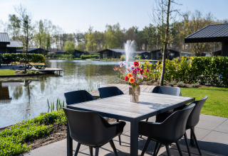 Udendørs spiseområde ved sø med springvand, moderne sorte stole og vase med blomster ved Villa Waterzicht Luxe 6.