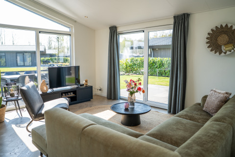 Helles, modernes Wohnzimmer in der Villa Waterzicht Luxe 6 im Ferienpark Molenvelden mit Gartenblick.