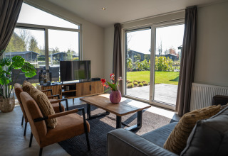 Sala moderna en Villa Waterzicht Luxe 6, Holiday park Molenvelden, con amplias ventanas y vista al jardín.