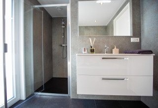 Moderne badeværelse med bruseniche, stort spejl, hvid vask og grå vægge i Villa Waterzicht Luxe 6.