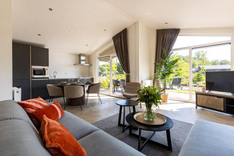 Moderne woonkamer in Villa Waterzicht Luxe met grote ramen, eethoek en tuinzicht op vakantiepark Molenvelden.