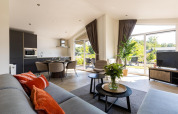Salon moderne de la Villa Waterzicht Luxe avec grandes baies, coin repas, TV et vue sur le jardin à Molenvelden.