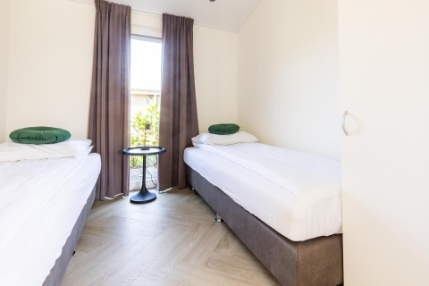 Dormitorio luminoso con dos camas individuales, cojines verdes y ventana en Villa Waterzicht Luxe, Molenvelden.