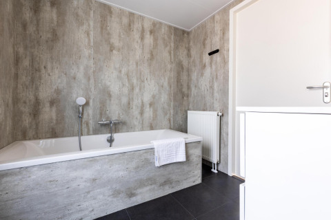 Salle de bain moderne avec une baignoire, murs gris texturés et sol foncé à la Villa Waterzicht Luxe.