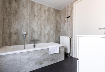 Modernes Badezimmer mit freistehender Badewanne, grauen Wänden und dunklem Boden in Villa Waterzicht.