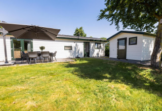 White Lodge mit Terrasse und Sonnenschirm im Holiday Park Molenvelden, Niederlande, grüne Umgebung.