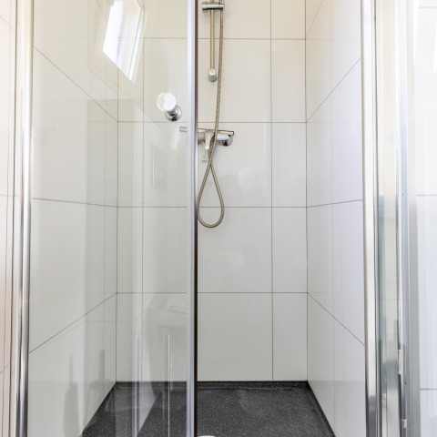 Modern shower cabin with glass doors and white tiles at White Lodge, Holiday park Molenvelden, Netherlands.