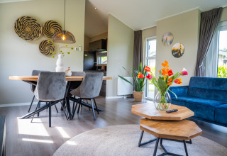 Modern living room in Wood Lodge Waterzicht with wooden decor, blue sofa and flowers at Molenvelden, Netherlands.