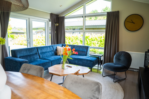 Stue i Wood Lodge Waterzicht med blå sofa, stort vindue og moderne indretning i Molenvelden, Holland.