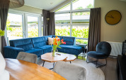 Wohnzimmer in Wood Lodge Waterzicht mit blauer Couch, großen Fenstern und moderner Einrichtung in Molenvelden.