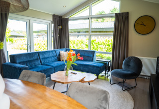 Soggiorno della Wood Lodge Waterzicht con divano blu, ampie finestre e arredi moderni a Molenvelden, Olanda.