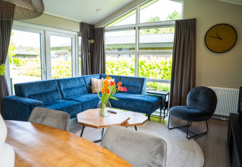 Salón en Wood Lodge Waterzicht con sofá azul, grandes ventanales y decoración moderna en Molenvelden, Países Bajos.