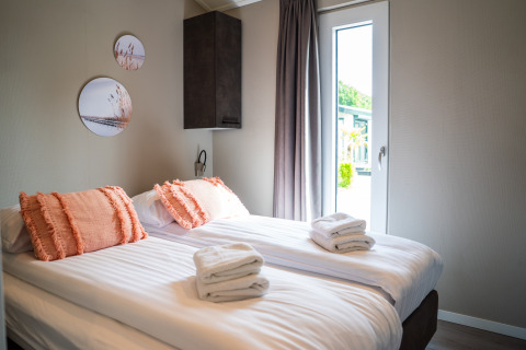 Modern bedroom with two single beds, orange pillows, and fresh towels in Wood Lodge Waterzicht, Molenvelden.